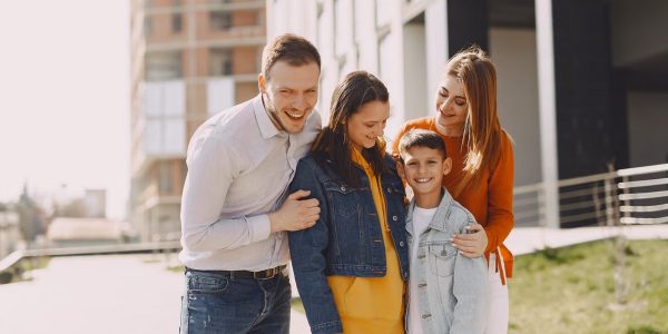 Delighted family in trendy casual wear holding each other and standing near modern building on city street while walking together during weekend