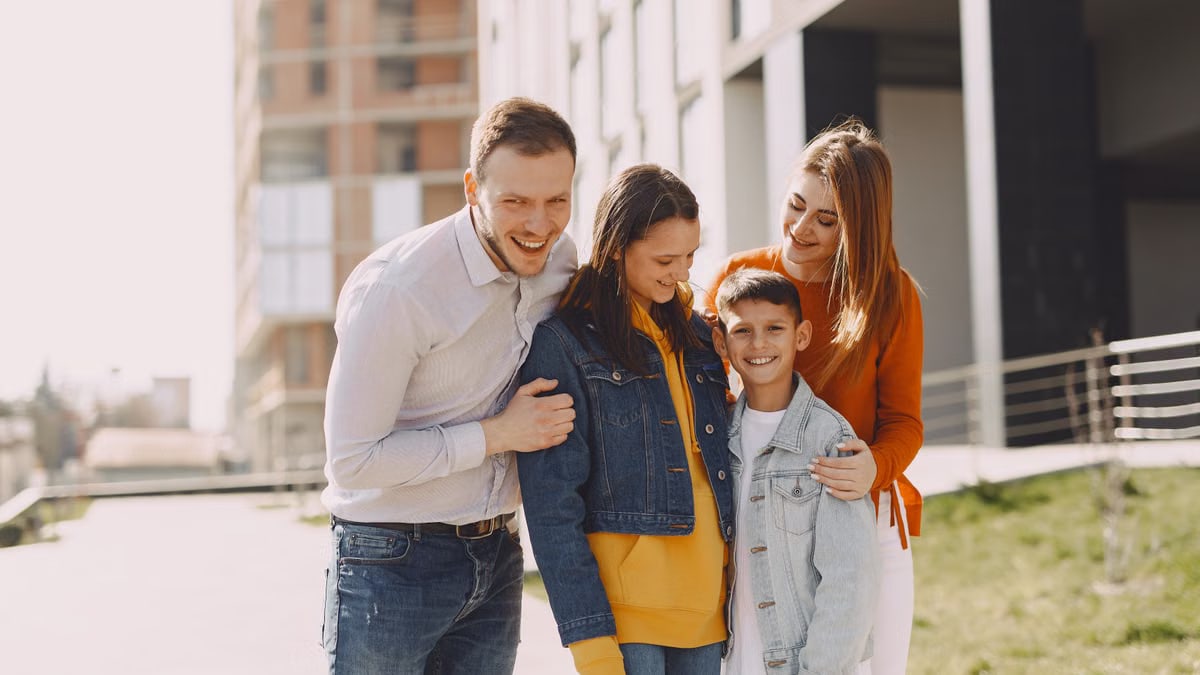 Delighted family in trendy casual wear holding each other and standing near modern building on city street while walking together during weekend