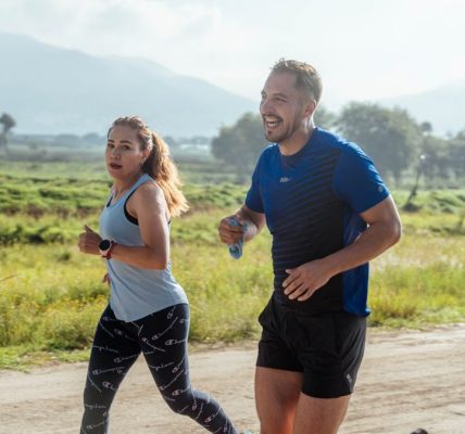 Two adults running on a rural dirt path, enjoying a sunny day outdoors.